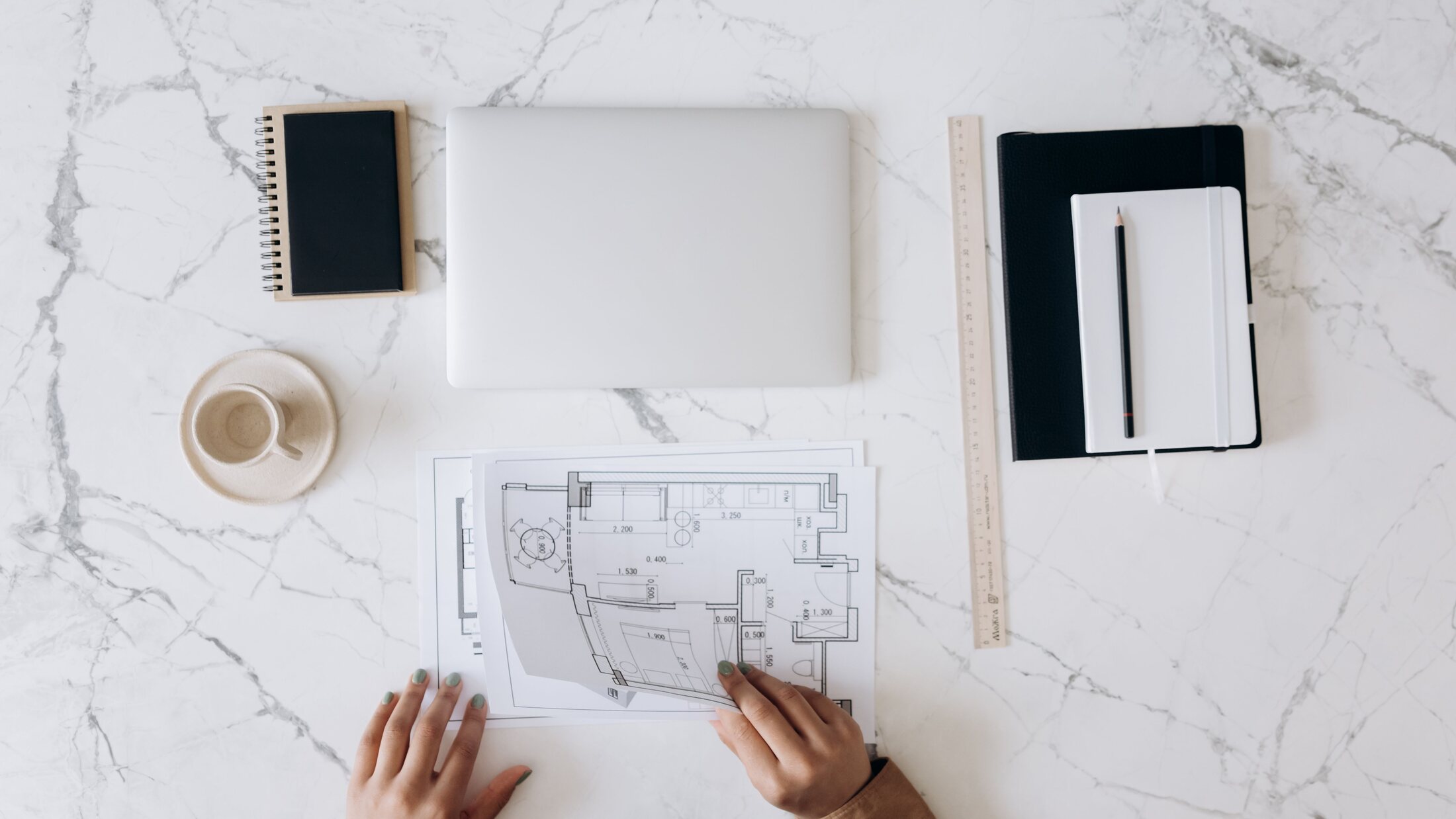 Architectural plans, laptop and drawing tools arranged across a designer's desk